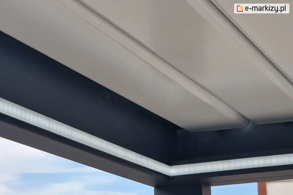 Belki zwieńczenia pergoli SB400 z zamontowanym oświetleniem led w formie taśmy pod złożonym dachem z białych lameli aluminiowych