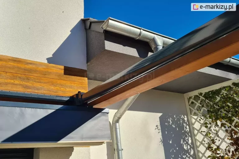 Pergola drewniana Koro z dachem Silva zbliżenie na prowadnicę międzyścienną, w tle widoczne zakończenie spadzistego dachu z cynkowaną rynną oraz pergola porośnięta zielonym bluszczem.
