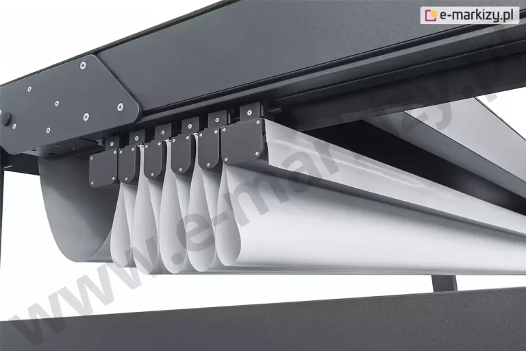 Zdjęcie prezentuje szczegółowe zbliżenie na mechanizm zwijania poszycia w produkcie pergola Solid Aluprof, ukazując sposób układania się tkaniny pod kasetą osłonową. Na pierwszym planie widoczny jest system aluminiowych profili poprzecznych w kolorze antracytowym, które są zakończone estetycznymi, czarnymi zaślepkami montowanymi na śruby. Do profili zamocowana jest wysokiej jakości biała tkanina techniczna, która po złożeniu dachu tworzy regularne, pionowe fałdy o zaokrąglonych krawędziach, przypominające estetykę rzymskiej rolety. Poszycie przesuwa się wzdłuż czarnych prowadnic bocznych zintegrowanych z ramą pergoli. Konstrukcja ramy charakteryzuje się matowym wykończeniem o drobnej strukturze. Widoczne są również detale techniczne, takie jak masywna boczna blacha montażowa z ozdobnymi śrubami, która stabilizuje połączenie prowadnic z kasetą dachu. Całość kompozycji na jasnym tle podkreśla nowoczesny design i precyzję wykonania ruchomych elementów systemu pergola Solid Set.