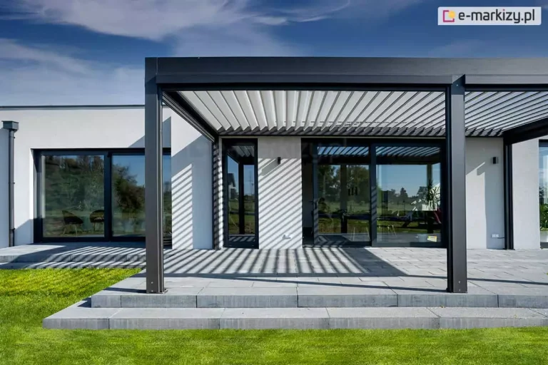 Opcjonalna podpora środkowa może okazać się niezbędna do montażu refleksoli, czyli dodatkowych osłon bocznych. Pergola SB400 Aluprof w dwóch kolorach współgra z kolorystyką otoczenia oraz nowoczesną bryłą parterowego budynku o jasnej elewacji i ciemnych ramach dużych przeszkleń.