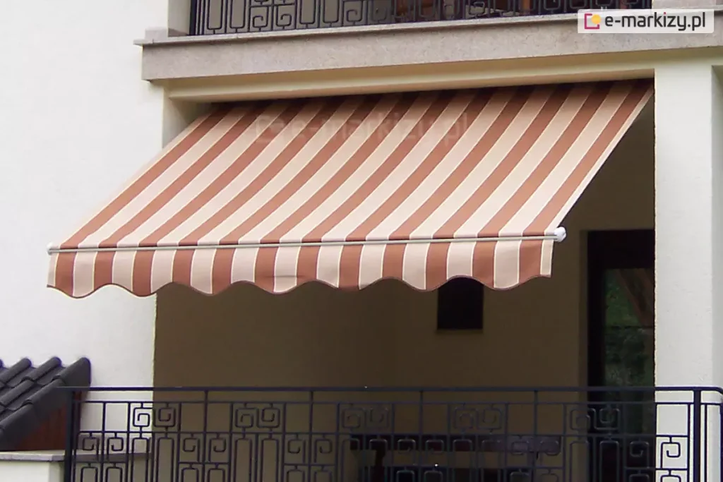 Zdjęcie prezentuje montaż markizy Piano MOL do sufitu. Na obrazie przedstawiono klasyczną markizę Piano na balkon, zamontowaną we wnęce loggii nowoczesnego, białego budynku mieszkalnego. Poszycie markizy wykonane jest z trwałej tkaniny w szerokie, pionowe pasy w kolorach ceglanego brązu oraz jasnego beżu, co tworzy elegancki kontrast z jasną elewacją. Materiał jest w pełni rozwinięty i napięty na konstrukcji, skutecznie osłaniając przestrzeń balkonu przed słońcem. Przednia krawędź, jaką posiada markiza Piano na balkon, wykończona jest ozdobną falbaną o falistym kształcie, obszytą lamówką dopasowaną kolorystycznie do ciemniejszych pasów tkaniny. Aluminiowy profil frontowy oraz widoczne zaślepki boczne są polakierowane na czysty, biały kolor. Poniżej linii markizy widoczna jest ozdobna, czarna balustrada balkonowa o geometrycznym wzorze, a powyżej znajduje się fragment kolejnego balkonu z podobną barierką. Markiza Piano na balkon została zainstalowana pod stropem wyższej kondygnacji, co zapewnia stabilność montażu i estetyczne domknięcie wnęki balkonowej.