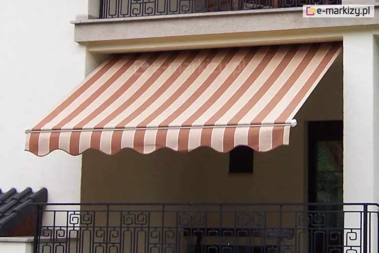 Zdjęcie prezentuje montaż markizy Piano MOL do sufitu. Na obrazie przedstawiono klasyczną markizę Piano na balkon, zamontowaną we wnęce loggii nowoczesnego, białego budynku mieszkalnego. Poszycie markizy wykonane jest z trwałej tkaniny w szerokie, pionowe pasy w kolorach ceglanego brązu oraz jasnego beżu, co tworzy elegancki kontrast z jasną elewacją. Materiał jest w pełni rozwinięty i napięty na konstrukcji, skutecznie osłaniając przestrzeń balkonu przed słońcem. Przednia krawędź, jaką posiada markiza Piano na balkon, wykończona jest ozdobną falbaną o falistym kształcie, obszytą lamówką dopasowaną kolorystycznie do ciemniejszych pasów tkaniny. Aluminiowy profil frontowy oraz widoczne zaślepki boczne są polakierowane na czysty, biały kolor. Poniżej linii markizy widoczna jest ozdobna, czarna balustrada balkonowa o geometrycznym wzorze, a powyżej znajduje się fragment kolejnego balkonu z podobną barierką. Markiza Piano na balkon została zainstalowana pod stropem wyższej kondygnacji, co zapewnia stabilność montażu i estetyczne domknięcie wnęki balkonowej.