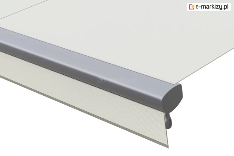 Zbliżenie na wykończenie krawędzi rozwiniętej markizy tarasowej Volant Aluprof. Zdjęcie przedstawia aluminiową belkę frontową o zaokrąglonym profilu w kolorze srebrno-szarym, w której zamontowana jest tkanina poszycia w kolorze złamanej bieli. Z dolnej części belki frontowej zwisa pionowa falbana markizowa o prostym kroju, wykonana z tego samego jasnego materiału. Po prawej stronie widoczna jest boczna zaślepka belki frontowej z wyprowadzonym pod nią szarym uchwytem lub elementem konstrukcyjnym. Tkanina markizy jest napięta płasko, ukazując gładką strukturę materiału. Całość zaprezentowana na jednolitym, jasnym tle.