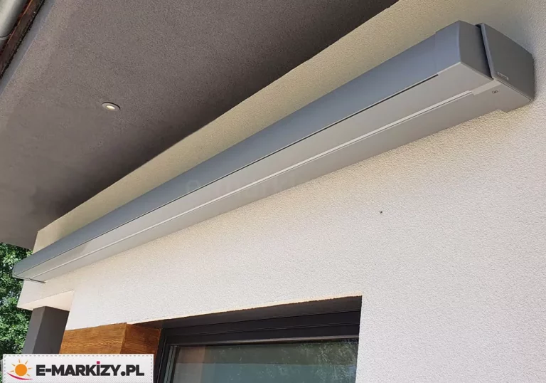 Markiza w pełnej kasecie Moderno MOL ze srebrna konstrukcją zamocowana do ściany o jasnym tynku strukturalnym pod okapem dachu w kolorze grafitowym.