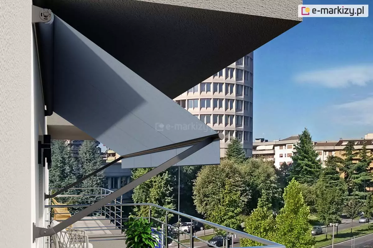 markiza Italia bez kasety Aluprof z antracytową konstrukcją oraz ramionami mocowanymi do ściany zawieszona nad wyjściem na taras, pod płytą balkonu wyższego piętra budynku. ramiona opuszczone pod katem około 50 stopni napinają szara tkaninę poszycia, która osłania wyjście na taras. W tle za tarasem widoczny balkon sąsiedniego mieszkania, ulica o średnim natężeniu ruchu częściowo przesłonięta licznymi drzewami oraz sąsiednie budynki, w tym widoczny na tle markizy wysoki obiekt o zaokrąglonej fasadzie.