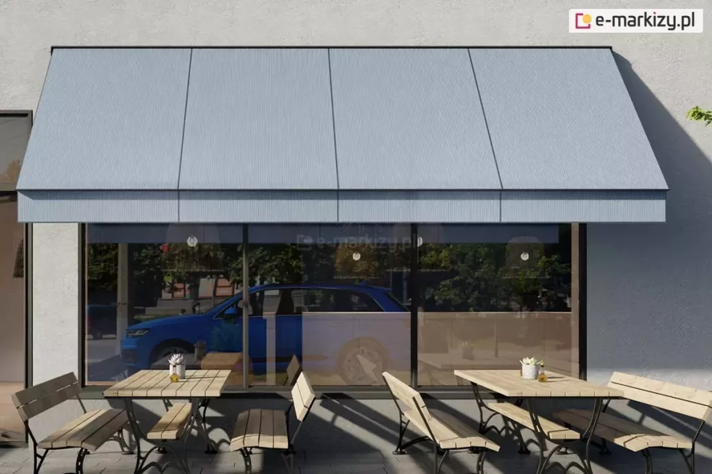Wizualizacja przedstawiająca nowoczesną markizę sklepową z ramionami opadowymi, zamontowaną nad witryną lokalu usługowego lub restauracji. Markiza posiada gładkie poszycie w kolorze jasnoszarym, które jest w pełni rozwinięte i nachylone pod stałym kątem, zapewniając ochronę przeciwsłoneczną. Konstrukcja wsporcza, obejmująca ramiona boczne oraz belkę frontową, wykonana jest z profili aluminiowych w kolorze czarnym lub bardzo ciemnym grafitowym. Ramiona są przymocowane do jasnej, tynkowanej elewacji budynku po obu stronach dużego przeszklenia. W witrynie odbija się fragment ulicy oraz zaparkowany przy krawężniku niebieski samochód typu SUV. Przed lokalem, na brukowanym podłożu, ustawiono drewniane stoliki kawiarniane z dopasowanymi ławami o metalowych, ozdobnych stelażach. Na stolikach znajdują się drobne akcesoria, takie jak białe doniczki z roślinami. Scena ukazuje słoneczny dzień, co podkreślają wyraźne, ukośne cienie rzucane przez meble oraz krawędź markizy na elewację i chodnik.