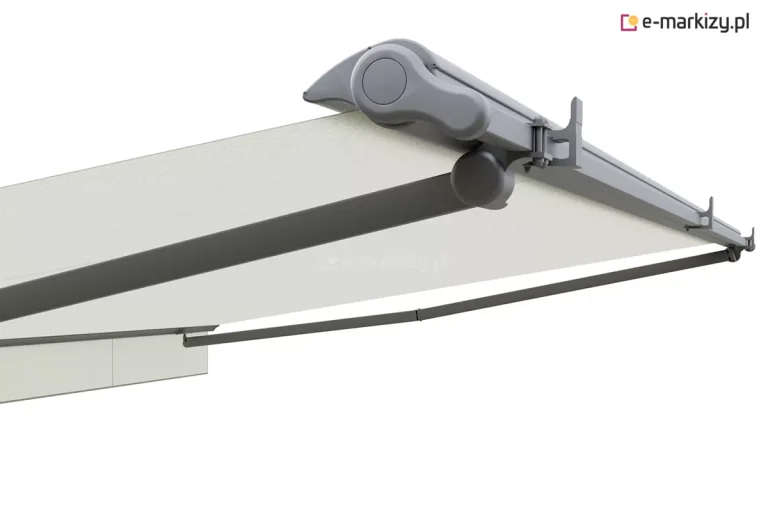 Zdjęcie prezentuje zbliżenie na mechanizm boczny oraz system konstrukcyjny markizy Adagio Mol w wersji z ciemnoszarą (antracytową) konstrukcją. Widoczna jest boczna pokrywa kasety o łagodnym, aerodynamicznym kształcie z charakterystycznym okrągłym przetłoczeniem na środku. Pod kasetą znajduje się masywny, zaokrąglony przegub ramienia, który jest połączony z długim, aluminiowym ramieniem podtrzymującym tkaninę. Poszycie markizy ma kolor jasnokremowy lub złamanej bieli i jest napięte między kasetą a profilem czołowym. Wzdłuż profilu belki montażowej widoczne są specjalistyczne uchwyty w kształcie odwróconej litery F, które służą do stabilizacji konstrukcji. System zamontowany jest na białej ścianie, a perspektywa ujęcia od dołu pozwala dostrzec solidność wykonania komponentów, takich jak aluminiowa belka kwadratowa stanowiąca rdzeń nośny markizy Adagio Mol. Całość charakteryzuje się nowoczesnym designem, gdzie ciemna kolorystyka metalowych elementów kontrastuje z jasnym materiałem osłonowym.