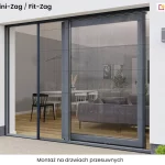 Grafika przedstawia produkt Fit-Zag moskitiera drzwiowa plisowana montaż zrealizowany na dwuskrzydłowych drzwiach przesuwnych tarasowych. Zdjęcie ukazuje produkt od strony zewnętrznej budynku, prezentując nowoczesną elewację w kolorze białym z ciemniejszym cokołem przy ziemi. System moskitiery składa się z ciemnoszarej ramy aluminiowej, która jest idealnie dopasowana do koloru stolarki otworowej. Po lewej stronie drzwi, w świetle przejścia, widoczna jest rozwinięta, czarna siatka o charakterystycznej strukturze plis (harmonijki), która jest utrzymywana w pionie przez cienki, czarny profil przesuwny. Druga część moskitiery pozostaje złożona przy ramie prawego skrzydła drzwiowego, które jest przeszklone i odbija wnętrze nowoczesnego salonu z widoczną kanapą, stołem jadalnianym oraz dekoracyjnymi lampami. Całość konstrukcji osadzona jest w dyskretnych prowadnicach: górnej zamontowanej pod nadprożem oraz dolnej, bardzo niskiej, przytwierdzonej do jasnego podłoża tarasu. Po obu stronach wnęki drzwiowej na ścianie zamontowano prostopadłościenne, szare kinkiety zewnętrzne. W dolnych rogach kadru widać niewielkie, zielone krzewy ozdobne w białej posypce kamiennej. Na górze obrazu umieszczono czarny tekst z nazwą modelu moskitiery, natomiast na dole znajduje się informacja o rodzaju montażu na drzwiach przesuwnych.