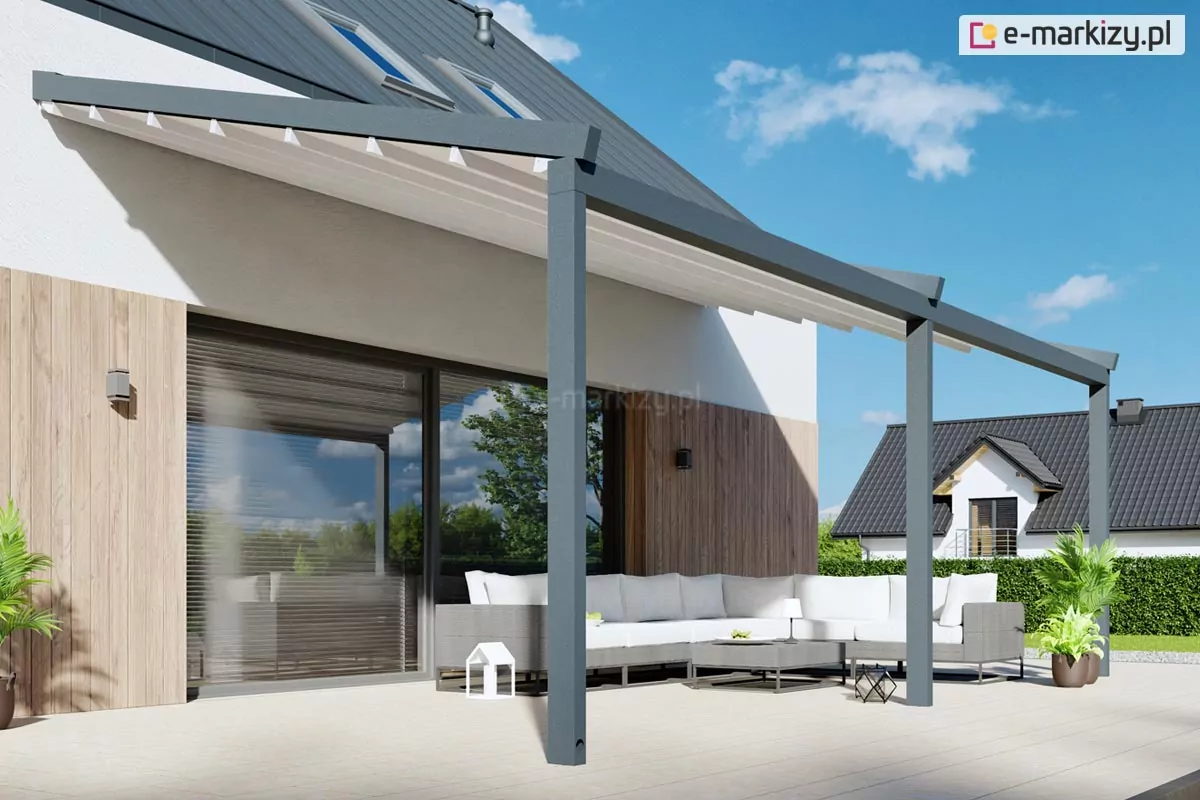 Nowoczesna pergola tarasowa dwumodułowa w kolorze antracytowym zamontowana do elewacji budynku jednorodzinnego, wyposażona w białe zadaszenie tkaninowe składane harmonijkowo. Konstrukcja opiera się na trzech pionowych słupach o przekroju kwadratowym, które podtrzymują prowadnice dachu zamontowane pod lekkim kątem nachylenia. Pod pergolą znajduje się jasny taras wyłożony dużymi płytami, na którym ustawiono narożny komplet wypoczynkowy w kolorze szarym z białymi poduszkami oraz niski stolik kawowy. W tle widoczna jest elewacja wykończona jasnym tynkiem i panelami drewnopodobnymi, duże przeszklenia przesuwne prowadzące do wnętrza domu oraz fragment ogrodu z niską roślinnością i sąsiednim budynkiem pod ciemnym dachem.