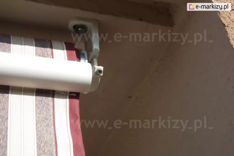Zbliżenie okrągłej belki przedniej markizy balkonowej poręczowej, do której przymocowane jest poszycie oraz falbana wykonane z tkaniny w pasy: bordowo-biało-kremowo-brązowe.
