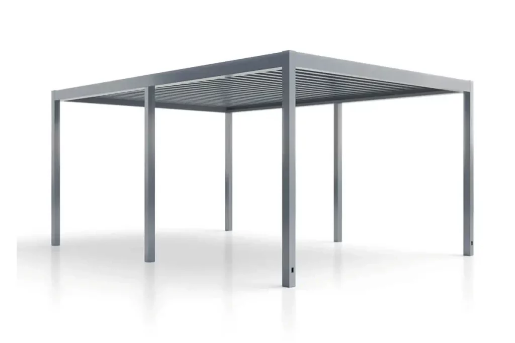 Nowoczesna, wolnostojąca pergola aluminiowa o wymiarach sześć na cztery metry model SB450 marki Aluprof, zaprezentowana na jednolitym, białym tle z widocznym, delikatnym odbiciem w podłożu. Cała konstrukcja, obejmująca prostokątną ramę górną oraz pionowe słupy podporowe o kwadratowym przekroju, jest wykonana z profilowanego aluminium pomalowanego proszkowo na jednolity, ciemnoszary kolor. Zadaszenie pergoli tworzy gęsty system poziomych, obrotowych lameli aluminiowych ułożonych równolegle obok siebie wewnątrz ramy. Konstrukcja opiera się na sześciu stabilnych słupach – czterech narożnych oraz dwóch dodatkowych słupach środkowych umieszczonych symetrycznie wzdłuż dłuższych boków ramy, co wzmacnia stabilność przy dużej rozpiętości. W dolnej części przednich słupów znajdują się małe, podłużne, czarne otwory przeznaczone do zintegrowanego odprowadzania wody opadowej z dachu. Kadr ukazuje produkt od przodu pod lekkim kątem od dołu, prezentując pełną przestrzeń pod zadaszeniem.
