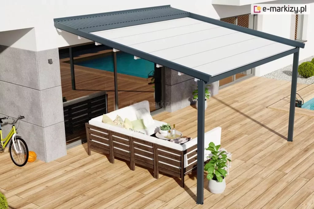 Widok z góry na nowoczesną pergolę Luxo o antracytowej konstrukcji, zamontowaną na przestronnym tarasie wyłożonym jasnymi deskami. Aluminiowa rama z zadaszeniem z białej, napiętej tkaniny chroni strefę wypoczynkową, w której ustawiono narożną sofę ogrodową z ciemnego drewna z białymi poduchami. Nad częścią materiału widoczny jest systemowy daszek ochronny z lamelami w kolorze konstrukcji, zabezpieczający poszycie po jego zwinięciu. W otoczeniu pergoli znajduje się basen, rower oparty o nowoczesną elewację budynku oraz donice z roślinami, co podkreśla rekreacyjny charakter przydomowej przestrzeni.