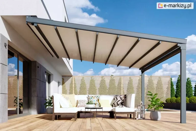 Pergola tarasowa Square z aluminiową konstrukcją w kolorze antracytowym zamocowaną poziomo do sufitu nad drzwiami tarasowymi. Jasne poszycie zapewnia ochronę przed słońcem i deszczem ustawionym na drewnianym tarasie meblom wypoczynkowym z białymi siedziskami oraz kolorowymi poduchami i stoliczkowi kawowemu z niską roślinką doniczkową pośrodku. Pod pergolą w pobliżu siedziska ustawiono donice z zielonymi roślinami oraz lampiony z jasnymi ramami. W tle widoczny drewniany trejaż, żywopłot przycięty w zielone kule oraz drzewa i błękitne niebo częściowo przesłonięte kłębiastymi chmurami.