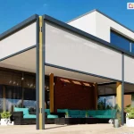 Pergola drewniana wolnostojąca z zabudową ziip na wszystkich ścianach pergoli skutecznie chroni przed nadmiernym nasłonecznieniem pomieszczenia oraz przestronny taras, na którym ustawiono ratanowe meble z turkusowymi poduchami i roślinki doniczkowe. Nad pergolą widoczne piętro nowoczesnego budynku oraz niebieskie niebo.