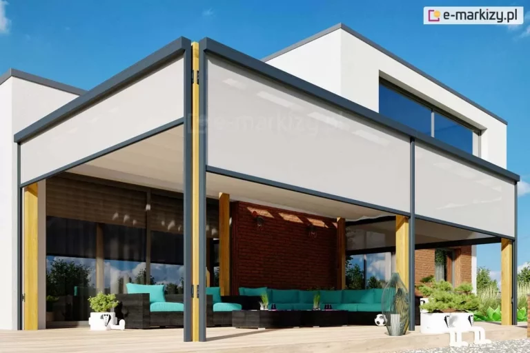 Pergola drewniana wolnostojąca z zabudową ziip na wszystkich ścianach pergoli skutecznie chroni przed nadmiernym nasłonecznieniem pomieszczenia oraz przestronny taras, na którym ustawiono ratanowe meble z turkusowymi poduchami i roślinki doniczkowe. Nad pergolą widoczne piętro nowoczesnego budynku oraz niebieskie niebo.