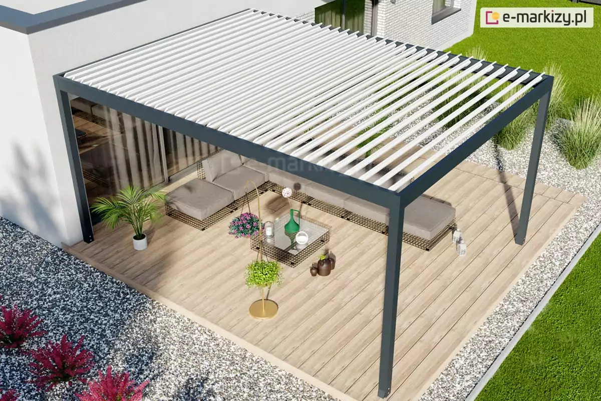 Nowoczesna pergola tarasowa w wersji wolnostojącej, zintegrowana z bryłą białego domu o minimalistycznej architekturze. Konstrukcja o antracytowym stelażu i białym dachu lamelowym osłania duży taras wyłożony deskami kompozytowymi w kolorze naturalnego drewna. Na tarasie znajduje się narożny zestaw wypoczynkowy z szarymi siedziskami, stolik kawowy oraz dekoracyjne rośliny w doniczkach, w tym palma i paproć. Otoczenie tarasu jest starannie zaprojektowane z wykorzystaniem jasnego żwiru, kęp traw ozdobnych oraz bordowych krzewów, a w oddali widać intensywnie zielony trawnik. Widok z góry pozwala na ekspozycję całego układu strefy relaksu oraz płynnego przejścia między wnętrzem domu a ogrodem.
