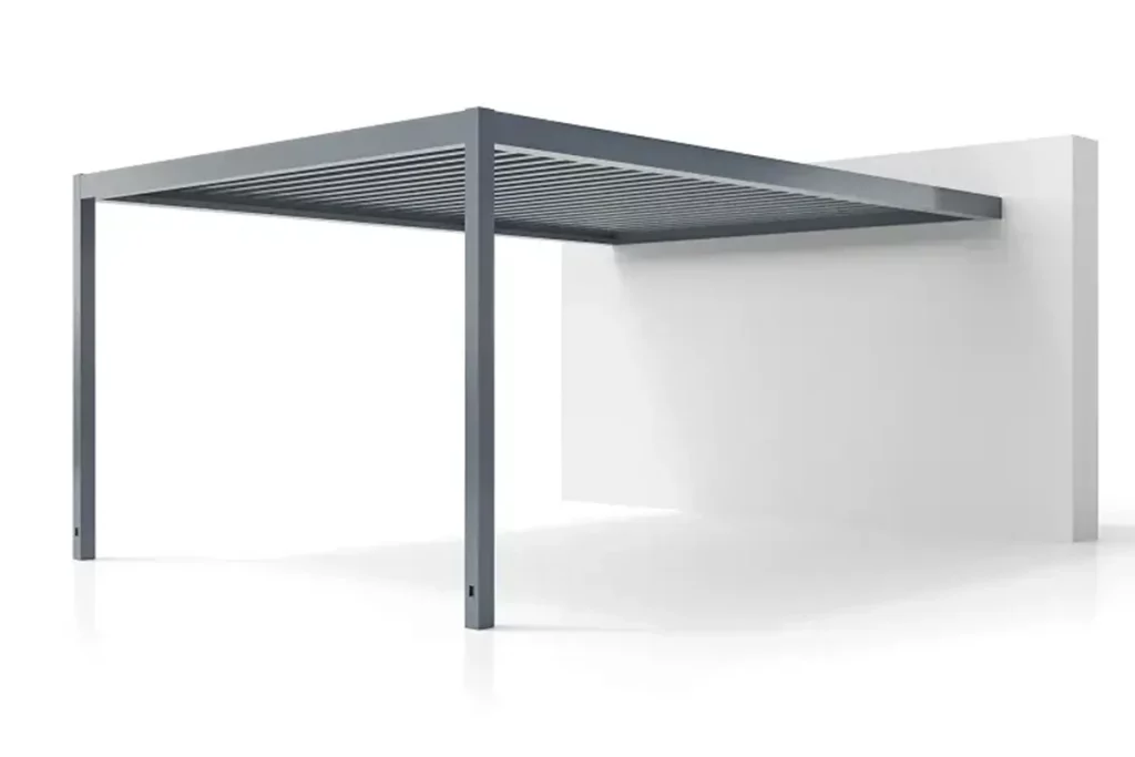 Wizualizacja produktowa przedstawiająca nowoczesną pergolę lamelową (bioklimatyczną) SB 450 w wersji przyściennej, zamontowaną jedną stroną do fragmentu białej ściany budynku. Konstrukcja pergoli wykonana jest z aluminium w kolorze ciemnoszarym (antracytowym) o matowym wykończeniu. Całość opiera się na dwóch pionowych, masywnych słupach nośnych o kwadratowym przekroju, które znajdują się na przedzie i stabilizują poziomą ramę zadaszenia. Zadaszenie składa się z ułożonych równolegle, ruchomych lameli aluminiowych (piór), które w tej pozycji są lekko uchylone, tworząc zwartą konstrukcję dachu. Produkt przedstawiony jest na jednolicie białym, jasnym tle z delikatnym odbiciem słupów i fragmentu ściany na podłożu, co nadaje całości minimalistyczny i techniczny charakter.