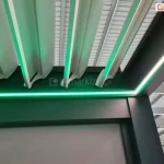 Pergola lamelowa z antracytową konstrukcją i białymi lamelami ze zintegrowanym oświetleniem LED w kolorze zielonym.