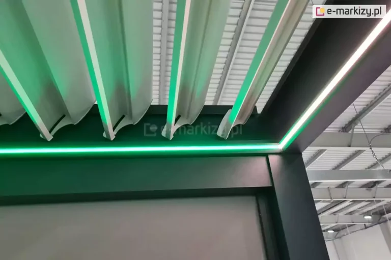 Pergola lamelowa z antracytową konstrukcją i białymi lamelami ze zintegrowanym oświetleniem LED w kolorze zielonym.