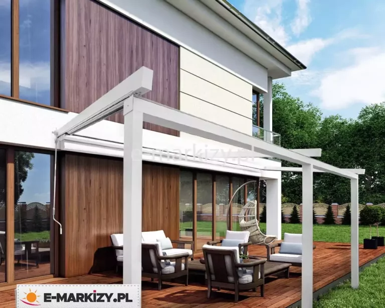 Duża, biała pergola modułowa Luxo, o szerokości siedmiu metrów zainstalowana przy nowoczesnym, piętrowym budynku z elewacją łączącą biel oraz panele o strukturze drewna. Konstrukcja opiera się na trzech masywnych, pionowych słupach nośnych, które podtrzymują długą belkę czołową oraz system bocznych prowadnic. Zadaszenie tkaninowe w kolorze białym jest w całości zwinięte pod daszek ochronny przy ścianie budynku, co w pełni odsłania przestronny taras wykonany z ciemnobrązowych desek. Na tarasie zaaranżowano strefę relaksu z kompletem mebli ogrodowych, w tym fotelami z jasnymi poduszkami oraz wiszącym fotelem typu kokon. Po lewej stronie konstrukcji widoczna jest manualna korba służąca do sterowania mechanizmem zadaszenia. W tle rozciąga się zadbany trawnik, niskie krzewy w czarnych donicach oraz ozdobne ogrodzenie, a całość doświetla naturalne światło dzienne pod lekko zachmurzonym niebem.