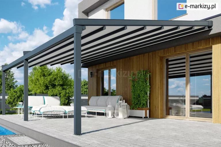 Nowoczesna wizualizacja pergoli tarasowej o grafitowej, aluminiowej konstrukcji, zamontowanej do elewacji budynku wykończonej pionowymi lamelami z jasnego drewna. Zadaszenie składa się z białego, segmentowego materiału rozpiętego na poprzecznych profilach, rzucającego głęboki cień na strefę wypoczynkową. Konstrukcja wspiera się na dwóch solidnych, kwadratowych słupach bocznych posadowionych na tarasie z jasnoszarej kostki brukowej. Pod pergolą znajduje się zestaw nowoczesnych mebli ogrodowych: biała sofa z jasnobłękitnym oblamowaniem oraz pasujące do niej niskie szezlongi i stolik kawowy. Dekorację stanowią dwie duże, białe ażurowe lampiony ustawione na ziemi oraz wysoka donica z zieloną ścianą roślinną przy elewacji. W tle widoczne są duże przeszklenia drzwi tarasowych, w których odbija się błękitne niebo z białymi chmurami, oraz fragment basenu po lewej stronie kadru. Scena przedstawia słoneczny dzień, co podkreśla kontrast między jasnymi meblami a ciemną ramą pergoli.