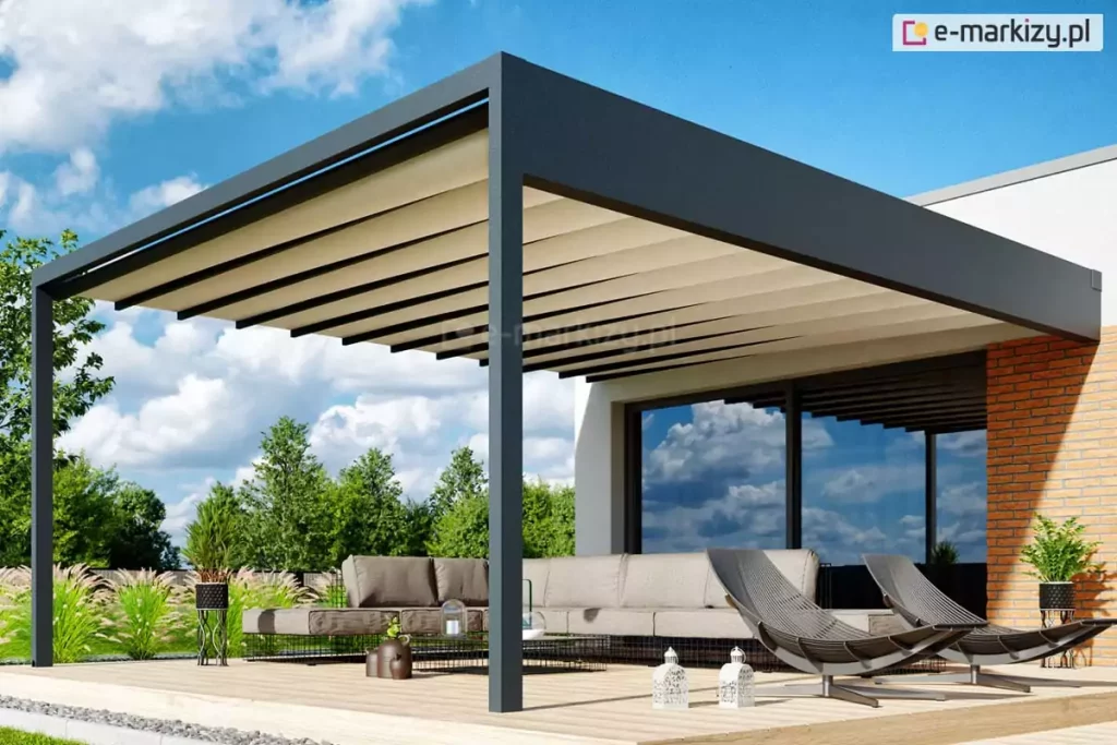 Zdjęcie prezentuje wizualizację luksusowej pergoli tarasowej Luxury o nowoczesnej, minimalistycznej konstrukcji aluminiowej w kolorze antracytowym. Zadaszenie stanowi dach tkaninowy w odcieniu jasnego beżu, który jest rozsunięty, tworząc miękkie, horyzontalne fale materiału rozpięte na prowadnicach. Konstrukcja wspiera się na solidnych profilach o kwadratowym przekroju i jest zamontowana do białej elewacji budynku z fragmentem wykonanym z czerwonej cegły. Pod pergolą, na jasnym drewnianym tarasie, zaaranżowano strefę wypoczynkową z dużym, niskim narożnikiem w kolorze taupe oraz dwoma designerskimi, ażurowymi fotelami w ciemnej tonacji. W przeszkleniach budynku odbija się błękitne niebo z białymi chmurami, a otoczenie tarasu wypełnia starannie wypielęgnowany ogród z ozdobnymi trawami i drzewami. Całość aranżacji uzupełniają stylowe detale, takie jak nowoczesne donice z roślinami oraz białe lampiony dekoracyjne ustawione na deskach tarasowych.