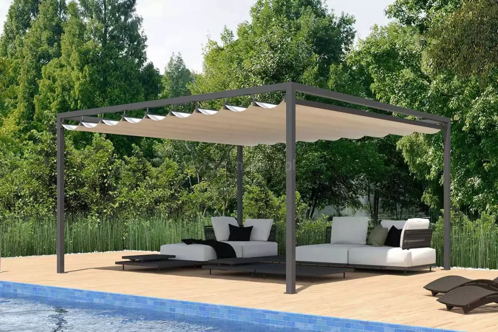 Wizualizacja wolnostojącej pergoli ogrodowej o minimalistycznej, antracytowej konstrukcji aluminiowej, ustawionej na jasnym, drewnianym tarasie przy basenie. Pergola tarasowa Dragon wolnostojąca posiada dach wykonany z jasnobeżowej tkaniny akrylowej, który jest rozłożony, tworząc regularne, dekoracyjne pofalowania między poprzecznymi profilami prowadzącymi. Pod pergolą zaaranżowano nowoczesną strefę wypoczynkową z białymi, niskimi modułowymi sofami ozdobionymi ciemnymi poduszkami. Meble spoczywają na płaskich, czarnych platformach, które pełnią funkcję zintegrowanych stolików bocznych. W dolnej części kadru widoczny jest fragment basenu z błękitną mozaiką oraz dwa brązowe, ergonomiczne leżaki ustawione na brzegu tarasu. Tło stanowi gęsta ściana wysokich, zielonych drzew oraz pas niskich traw ozdobnych, które oddzielają strefę tarasu od naturalnego krajobrazu. Całość ujęcia prezentuje się w pełnym, dziennym świetle, podkreślając luksusowy charakter letniej strefy relaksu.