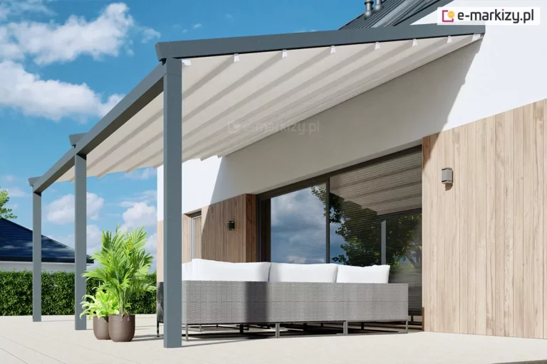 Wizualizacja prezentująca produkt pergola przyścienna Moderno zainstalowaną na nowoczesnym tarasie, ukazana pod kątem z perspektywy bocznej. Konstrukcja pergoli w kolorze ciemnego antracytu jest zamocowana do białej ściany budynku, która została ozdobiona pionowymi panelami o teksturze jasnego drewna. Zadaszenie stanowi jasna, kremowa tkanina ułożona w estetyczne fałdy, rozpięta na poprzecznych profilach, w których zamontowano zintegrowane punkty oświetlenia LED. Całość konstrukcji wspiera się na trzech solidnych, kwadratowych słupach nośnych, ustawionych na jasnym, gładkim podłożu tarasu. Pod pergolą znajduje się długa, szara sofa technorattanowa z białymi poduszkami oparciowymi, ustawiona tyłem do dużego przeszklenia drzwi tarasowych, w których odbija się błękitne niebo i okoliczna zieleń. Po lewej stronie, obok konstrukcji, stoją dwie brązowe donice z bujnymi zielonymi roślinami, w tym palmą. W tle widoczny jest fragment dachu sąsiedniego budynku oraz zielony żywopłot, a nad całością roztacza się pogodne niebo z lekkimi chmurami.