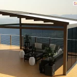Nowoczesna pergola tarasowa wolnostojąca Square MOL o konstrukcji aluminiowej, zlokalizowana na rozległym tarasie z widokiem na góry. Pergola posiada jednospadową konstrukcję, pod którą zamontowany jest tkaninowy dach, z jasnej, w pełni rozsuniętej tkaniny, osłaniającej strefę wypoczynkową. Konstrukcja pergoli w kolorze antracytu wspiera się na solidnych pionowych słupach i poziomych belkach. Dwie ściany obiektu są przeszklone przy użyciu bezramowego systemu przesuwnych szyb, przy czym ściany te wykonane są z przyciemnianego, ciemnego szkła, co zapewnia prywatność i ochronę przed słońcem. Wewnątrz pergoli znajduje się luksusowy zestaw mebli ogrodowych, w tym narożna sofa w kolorze grafitowym z jasnymi poduszkami, czarny stolik kawowy oraz białe, ażurowe pufy w kształcie bębnów. Całość uzupełniają rośliny doniczkowe w czarnych, dekoracyjnych donicach. Taras wyłożony jest deskami kompozytowymi w jasnym, naturalnym odcieniu drewna i zabezpieczony minimalistyczną balustradą ze stali nierdzewnej z poziomymi relingami. W tle rozpościera się panoramiczny widok na zamglone pasma górskie pod jasnym, bezchmurnym niebem, co podkreśla ekskluzywny charakter realizacji.