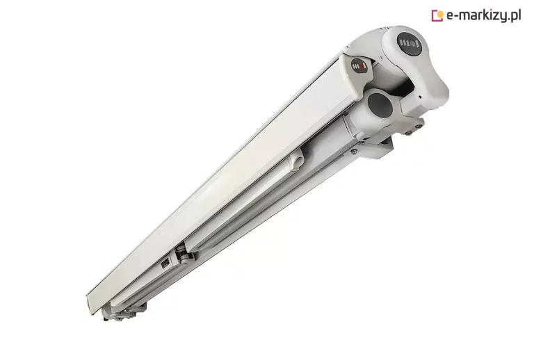 Zdjęcie prezentuje na białym tle spód konstrukcji osłony przeciwsłonecznej, którą jest markiza Tremolo w wersji półkasetowej. Biały, aluminiowy stelaż jest ukazany w pozycji złożonej pod kątem od dołu, co uwidacznia sposób, w jaki profil czołowy domyka górną część kasety, chroniąc zwinięty materiał. Widoczne są solidne przeguby ramion oraz boczna pokrywa o nowoczesnym kształcie z ciemnym elementem dekoracyjnym. Całość konstrukcji charakteryzuje się czystą linią i brakiem widocznych rur nawojowych od spodu, co potwierdza wysoką estetykę i funkcjonalność domykającego mechanizmu kasetowego.
