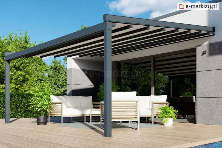 Nowoczesna pergola tarasowa Square o konstrukcji aluminiowej w kolorze ciemnego antracytu, zamontowana do białej elewacji piętrowego budynku o minimalistycznej architekturze. Zadaszenie pergoli wykonane jest z jasnego, kremowego materiału rozpiętego na poprzecznych profilach, które tworzą pod spodem wyraźny, regularny wzór pasów. Konstrukcja wspiera się na dwóch solidnych słupach o kwadratowym przekroju, ustawionych na przestronnym tarasie wyłożonym płytami gresowymi imitującymi jasne drewno. Pod pergolą zaaranżowano strefę wypoczynkową z szarym narożnikiem ogrodowym ozdobionym jasnymi poduszkami oraz zestawem jadalnianym z krzesłami o technorattanowej plecionce. Wokół tarasu znajduje się niski, biały murek pełniący funkcję donicy, w której posadzono ozdobne trawy i niskie krzewy. W tle widoczny jest zadbany trawnik, gęsty żywopłot z tui oraz wysokie drzewa iglaste pod czystym, błękitnym niebem. Duże przeszklenia budynku z ciemnymi ramami odbijają otaczającą zieleń.