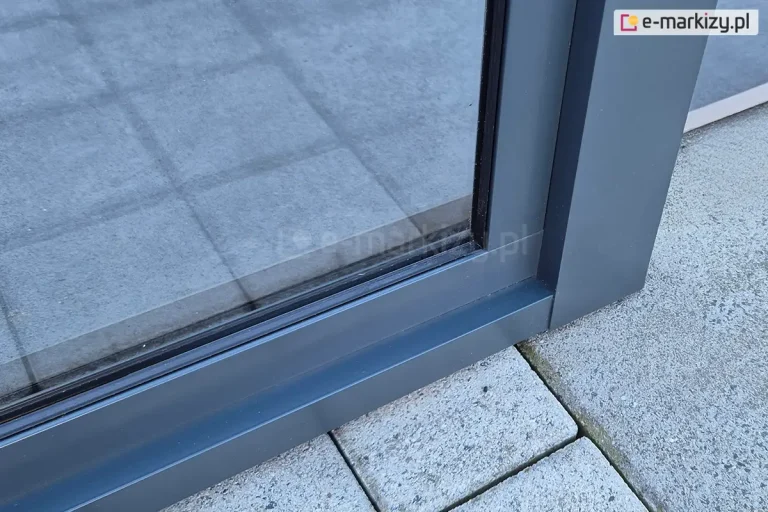 Dodatkowa rama, do której zamocowano stałe okno do zadaszeń fest stanowi wzmocnienie konstrukcji i element dekoracyjny zadaszenia. Antracytowa konstrukcja postawiona została na tarasie z betonowych kostek i płyt.