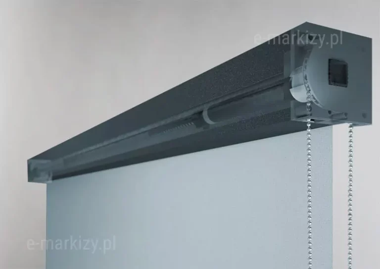 Trójwymiarowa wizualizacja techniczna ukazująca wewnętrzny mechanizm sterujący systemu refleksol 85MA Aluprof w dużym przybliżeniu. Zdjęcie prezentuje przekrój boczny kasety o barwie ciemnego antracytu z matowym wykończeniem, w której boczna i frontowa ścianka zostały przedstawione jako półprzezroczyste, aby odsłonić detale konstrukcyjne. Wewnątrz obudowy widoczny jest mechanizm napędowy z kołem zębatym, przez które przewieszony jest srebrny łańcuszek kulkowy służący do ręcznej obsługi rolety. Łańcuszek zwisa pionowo w dół przez otwór w dolnej części kasety. Z mechanizmu wyprowadzona jest rura nawojowa, na którą nawinięta jest jasnoszara tkanina techniczna ekranu. Konstrukcja mechanizmu jest precyzyjnie dopasowana do kwadratowego profilu kasety, a boczny dekiel posiada widoczne otwory na śruby montażowe. Całość ukazana jest na neutralnym, jasnym tle, co podkreśla techniczny charakter detalu i precyzję wykonania elementów sterujących systemu refleksol 85MA.