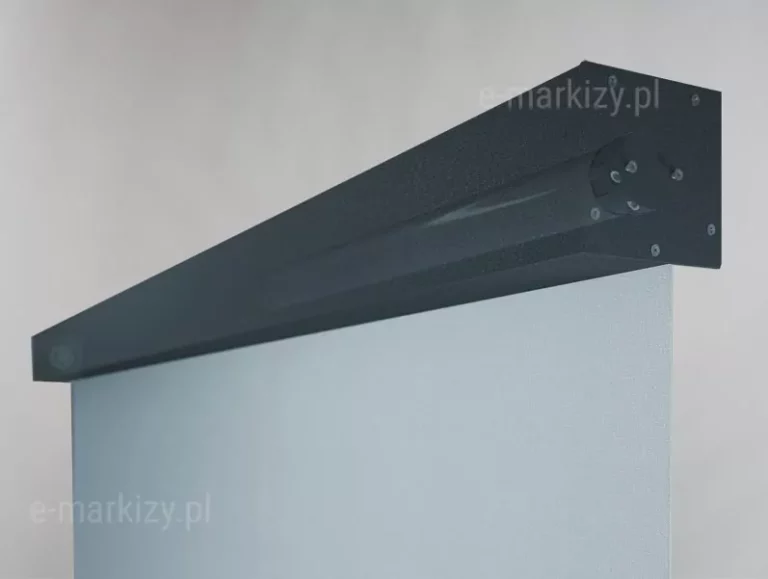 Zbliżenie na detale konstrukcyjne górnej części systemu refleksol 85, ukazujące kasetę oraz sposób wyprowadzenia tkaniny. Zdjęcie wykonane z perspektywy dolnej, bocznej, co pozwala na wyraźne dostrzeżenie tekstury materiałów. Aluminiowa kaseta o kwadratowym przekroju ma kolor głębokiego antracytu o drobnoziarnistej, matowej strukturze. W półprzezroczystym widoku ukazano zamocowany we wnętrzu rury nawojowej umieszczonej w kasecie silnik elektryczny do sterowania tkaniną osłony. Na bocznej pokrywie (deklu) kasety widoczne są precyzyjnie rozmieszczone cztery śruby montażowe z łbami krzyżakowymi, zabezpieczające mechanizm wewnętrzny. Z dolnej szczeliny kasety wysuwa się gładka, jasnoszara tkanina techniczna o drobnym splocie, która stanowi ekran osłony. Krawędź tkaniny jest idealnie prosta, co świadczy o precyzji mechanizmu zwijającego. Tło jest neutralne, jasnoszare, co sprawia, że ciemna bryła kasety oraz jasna płaszczyzna materiału są wyraźnie odseparowane i dobrze widoczne. Całość podkreśla techniczną jakość wykonania oraz nowoczesny design detali systemu refleksol 85.