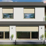 Zdjęcie prezentuje nowoczesny, dwukondygnacyjny budynek mieszkalny o minimalistycznej architekturze i jasnej elewacji, wyposażony w system zewnętrznych rolet typu screen w kolorze jasnego beżu. W górnej kondygnacji budynku znajdują się dwa symetrycznie umieszczone okna z drewnianymi ramami, częściowo zasłonięte roletami, w których widocznym odbiciu maluje się błękitne niebo z chmurami oraz korony drzew. Po prawej stronie piętra zaprojektowano otwarty taras z przeszkloną balustradą i widocznym segmentem drewnianej okładziny ściennej. Na parterze ulokowano duże, panoramiczne przeszklenia z widocznym wyjściem na przestronny, jasnoszary taras wyłożony płytami betonowymi, na którym rozmieszczono dekoracyjne rośliny w donicach oraz nowoczesny zestaw wypoczynkowy ze stołem i krzesłami ogrodowymi. Oknom i drzwiom tarasowym na parterze również towarzyszą zamontowane w górnych częściach kasety rolet screen, częściowo zacieniające wnętrza i redukujące wpadające promienie słoneczne. Bryłę budynku domyka ciemnoszara, grafitowa rama stropowa oraz attyka, tworząc wyrazisty kontrast z jasnymi ścianami. Wzdłuż tarasu widoczne są czarne, minimalistyczne oprawy oświetleniowe gruntowe, a przed budynkiem rozciąga się równo przycięty pas zielonego trawnika w pełnym świetle słonecznym.