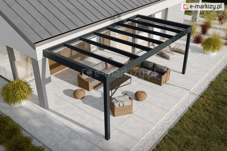 Wizualizacja przedstawia nowoczesną realizację zadaszenia tarasu Spekta Glass, zintegrowaną z bryłą minimalistycznego budynku jednorodzinnego o jasnej elewacji. Konstrukcja nośna została wykonana z profili aluminiowych w kolorze antracytowym, które tworzą ramę dachu opartą z jednej strony na ścianie budynku, a z drugiej na dwóch pionowych słupach. Dach konstrukcji jest w całości przeszklony i podzielony na regularne sekcje, co zapewnia pełną przezierność i ochronę przed warunkami atmosferycznymi. Pod zadaszeniem zaaranżowano strefę relaksu z meblami z technorattanu w odcieniu naturalnego brązu, obejmującą sofę, fotel oraz niskie pufy i stolik kawowy. Podłoże tarasu oraz opaskę wokół budynku stanowią wielkoformatowe płyty tarasowe w kolorze jasnoszarym, które są oddzielone od trawnika pasem białego gresu. Architektura ogrodu obejmuje również ozdobne trawy w białych donicach oraz nasadzenia wzdłuż elewacji, co tworzy spójną i estetyczną przestrzeń wypoczynkową.