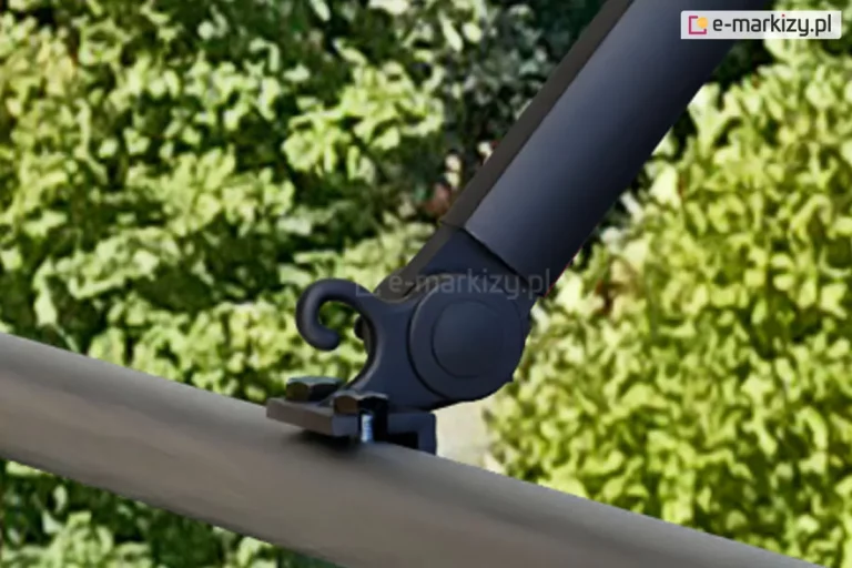 Zbliżenie sposobu mocowania czarnego ramienia markizy balkonowej poręczowej do okrągłej barierki balustrady tarasu. W tle widoczne rośliny o zielonych liściach.