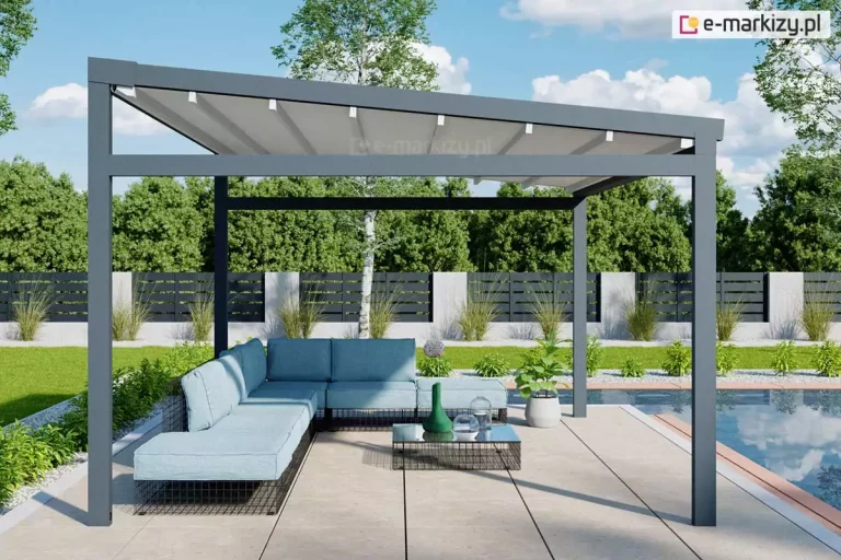 Zdjęcie prezentuje produkt pergola tarasowa wolnostojąca Moderno usytuowaną w nowoczesnej aranżacji ogrodowej przy basenie. Konstrukcja pergoli charakteryzuje się minimalistyczną formą, wykonaną z solidnych profili aluminiowych o kwadratowym przekroju w kolorze głębokiego antracytu. Zadaszenie stanowi jasny, kremowy materiał techniczny rozpięty na ruchomych poprzeczkach, który jest zamontowany pod lekkim skosem, co ułatwia odprowadzanie wody opadowej. Pod pergolą znajduje się strefa wypoczynkowa z dużym, narożnym meblem modułowym w kolorze jasnobłękitnym, ustawionym na podłożu z jasnych, wielkoformatowych płyt tarasowych. Obok sofy stoi niski, nowoczesny stolik kawowy z szklanym blatem, na którym umieszczono dekoracyjne naczynia. Tło kompozycji stanowi zadbany ogród z zielonym trawnikiem, niską roślinnością ozdobną oraz nowoczesnym ogrodzeniem panelowym w kolorze czarnym z betonowymi słupkami. Po prawej stronie kadru widoczna jest krawędź błękitnej tafli wody basenowej, a w oddali gęsta ściana drzew liściastych pod jasnym, lekko zachmurzonym niebem. Cała scena jest oświetlona naturalnym, dziennym światłem, podkreślającym detale wykończenia pergoli oraz fakturę materiałów.