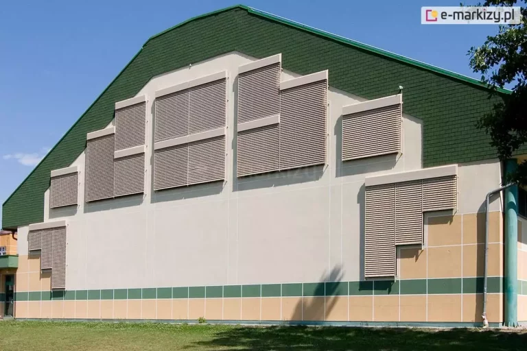 Okna osłonięte żaluzjami fasadowymi Z90 Oval w różnych wymiarach tworzą regularną, interesującą dekorację fasady wykończonej górą cegłami w kolorze intensywnej zieleni.