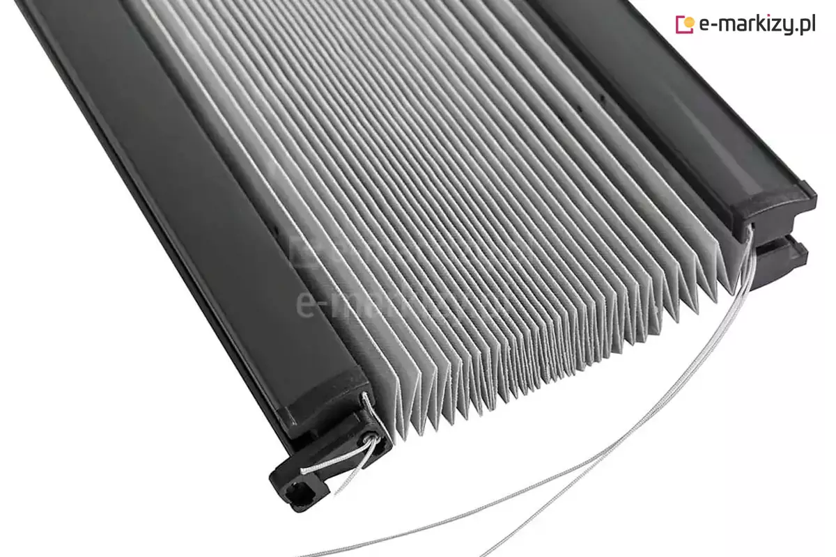 Zdjęcie przedstawia techniczne zbliżenie na produkt, którym jest żaluzja plisowana Plisa na okno posiada charakterystyczny materiał w kolorze jasnoszarym, zaprasowany w gęstą i regularną harmonijkę, która jest częściowo złożona. Tkanina żaluzji jest osadzona pomiędzy dwoma równoległymi, aluminiowymi profilami o matowym wykończeniu w odcieniu głębokiej czerni. Na końcach profili widoczne są precyzyjnie wykonane zatyczki z tworzywa sztucznego, które służą jako punkty kotwiczenia dla systemu sznurkowego. Przez te elementy przechodzą cienkie, wytrzymałe sznurki prowadzące w kolorze jasnoszarym lub srebrnym, które odpowiadają za stabilne utrzymanie osłony przy szybie oraz umożliwiają jej płynne przesuwanie w górę i w dół. Konstrukcja pokazana jest pod kątem na neutralnym, białym tle, co uwydatnia detale techniczne, takie jak sposób przewleczenia linek przez otwory w profilu oraz sztywność i geometrię zagięć materiału. Całość prezentuje nowoczesny design i solidną budowę systemu osłonowego, kładąc nacisk na estetykę połączenia metalu, tworzywa i tkaniny.