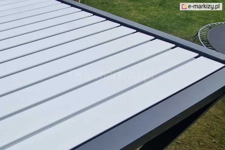 Złożone zadaszenie pergoli SB350 z systemem odprowadzania wody, pergola o antracytowej konstrukcji i białych lamelach ustawiona została na trawniku z widoczną w pobliżu trampoliną