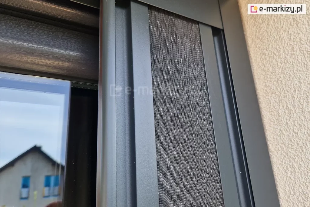 Moskitiera plisowana Top Zag z szarą siatką i antracytową konstrukcją po zwinięciu pakietu zajmuje niewielką przestrzeń we wnęce okiennej.