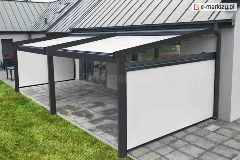 Pergola tarasowa Square ustawiona przy ścianie domku o jasnej betonowej fasadzie, nad tarasem z płyt betonowych, wyposażona w boczne osłony refleksol Zip L Zip U, które skutecznie chronią przestrzeń tarasu przed słońcem, deszczem, wiatrem i spojrzeniami sąsiadów. Przy tarasie zadbany trawnik.