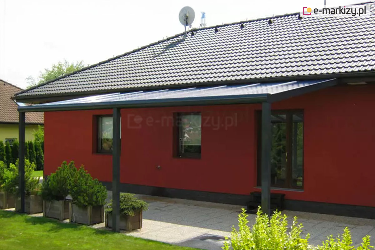 Nowoczesna konstrukcja zadaszenia z poliwęglanu w kolorze dachu budynku na tle ciemnoczerwonej ściany elewacji