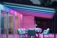 Kolorowe oświetlenie tarasu z zadaszeniem poliwęglanowym i meblami ogrodowymi z wygodnymi poduszkami