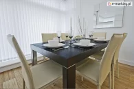 Jadalnia z mahoniowym stołem zastawionym na pięć osób i designerskim lustrem na ścianie osłonięta pionowymi białymi pasami tkaniny