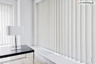 Biuro w odcieniach bieli z czarnym stolikiem i lampką na środku i roletami vertikal na wnękach okiennych