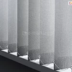 Szare pasy tkaniny w osłonie vertikal połączone łańcuszkami sterującymi tuż nad białym parapetem z zaokrąglonymi krawędziami