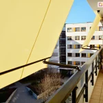 Żółta markiza balkonowa z mocowaniami do balustrady w kolorze brązowym na blokowisku