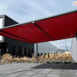 Pergola przyścienna Vera Sola na konstrukcji aluminiowej i zadaszeniem tkaninowym zacieniająca fragment placu